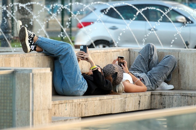 Jugendliche die auf einer Bank in der Stadt liegen und mit ihren Smartphones spielen
