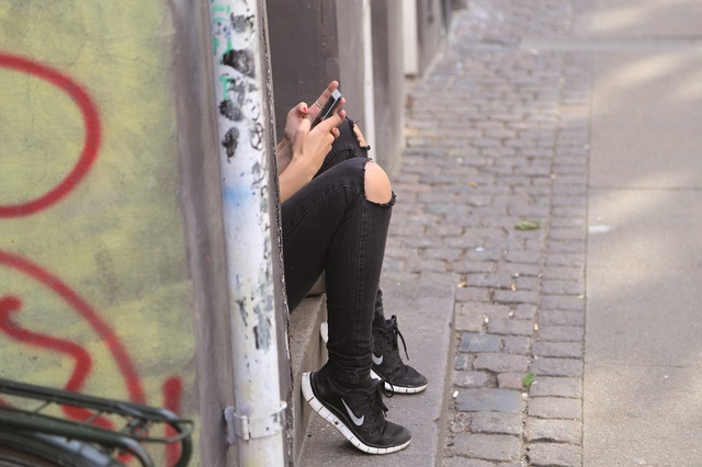 Beine einer Jungendlichen auf Bordsteinkante sitzend mit Handy